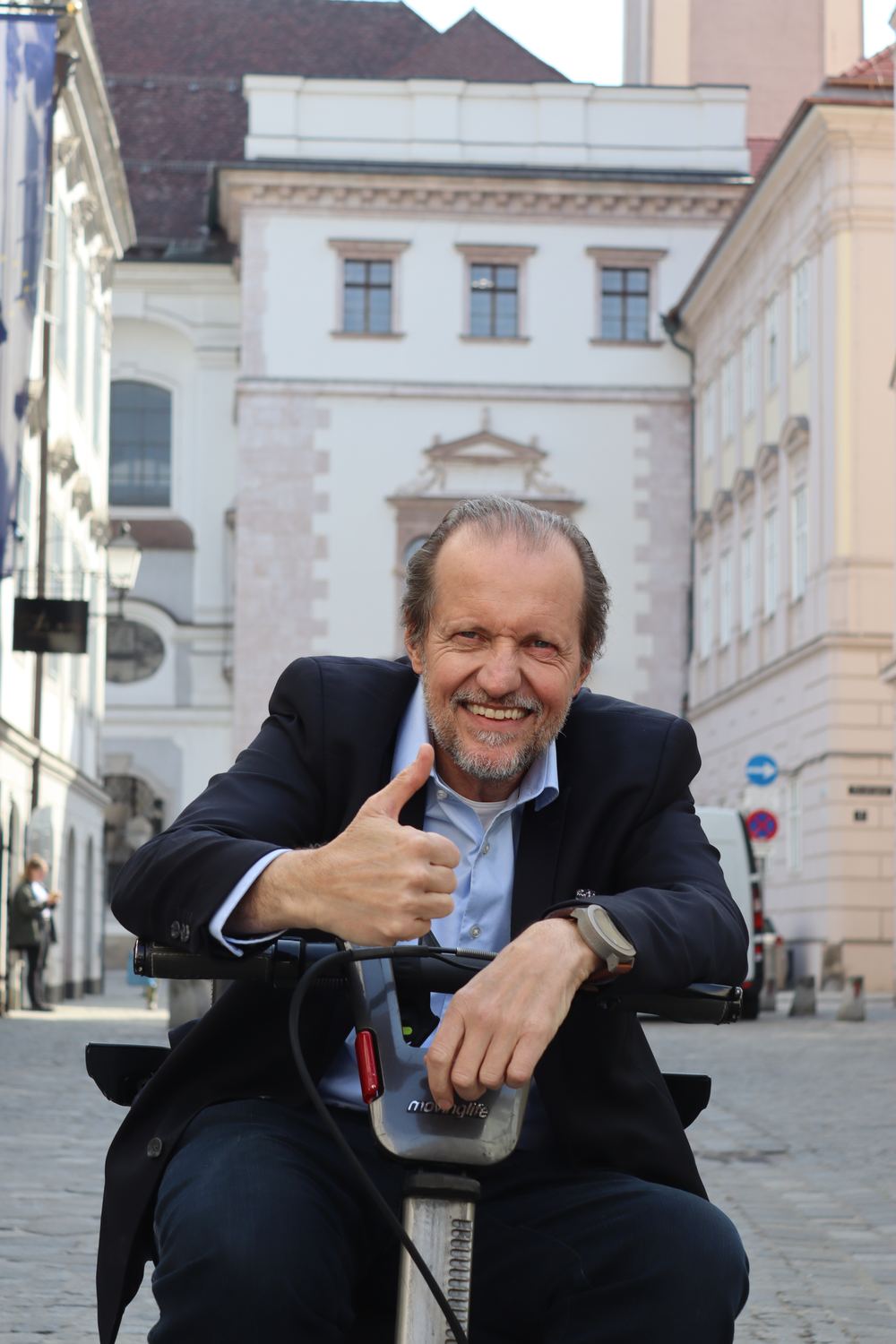 Georg Redlhammer auf seinem Roller in der Linzer Altstadt, er hebt lächelnd den Daumen