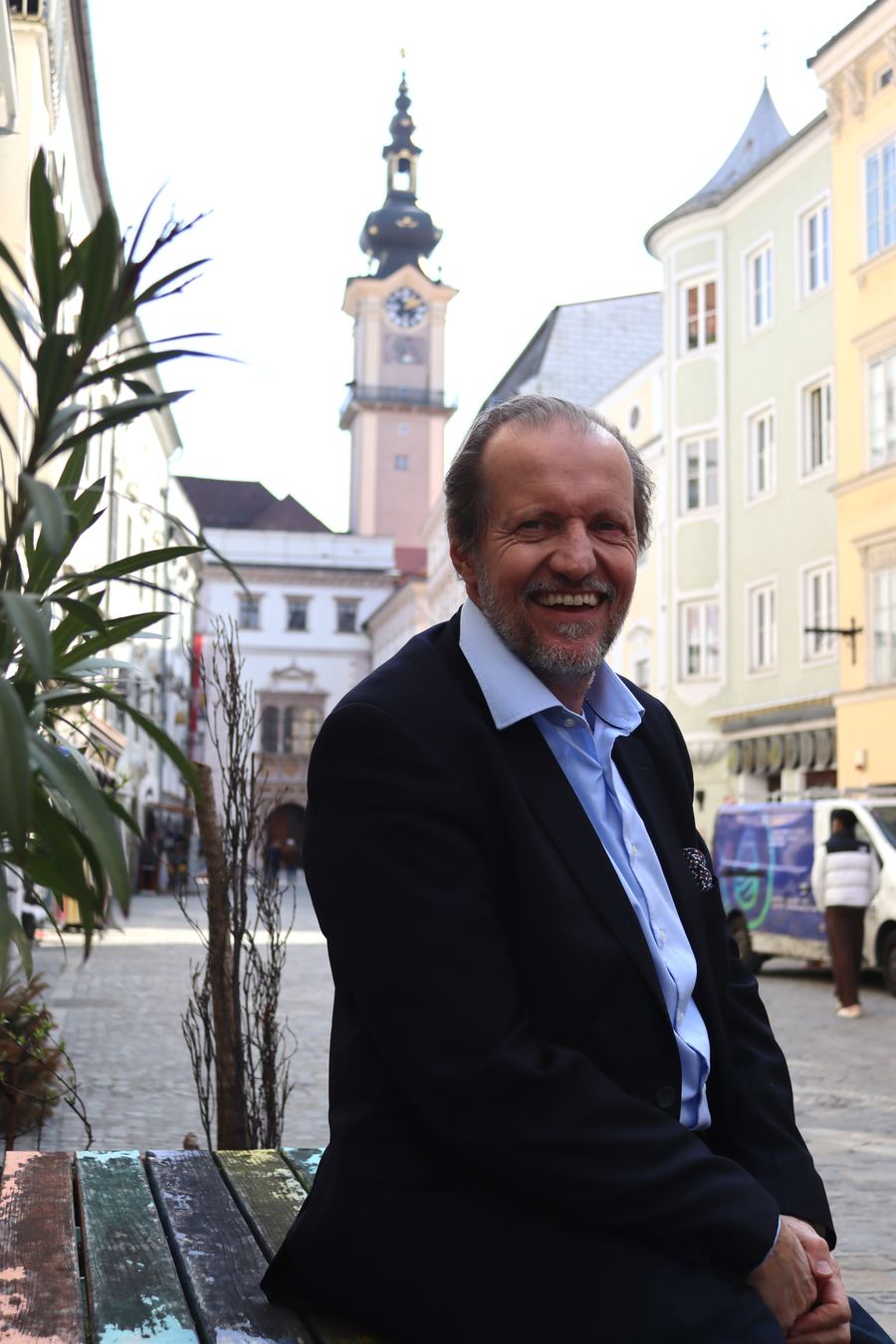 Georg Redlhammer sitzt auf einer Bank in der Linzer Altstadt und lächelt